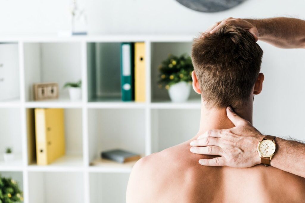 cropped view of doctor touching neck of shirtless patient sitting in clinic